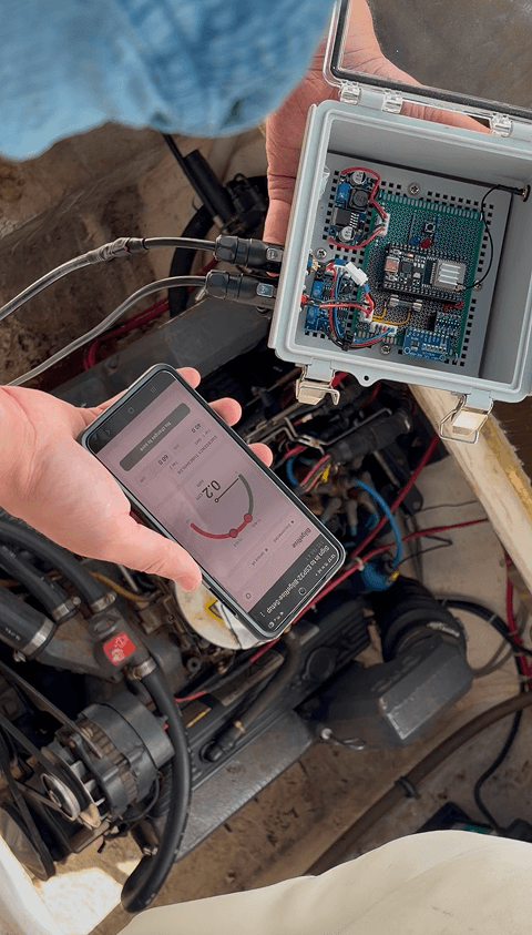 Phone showing BilgeRise water level beside the controller unit in a boat bilge
